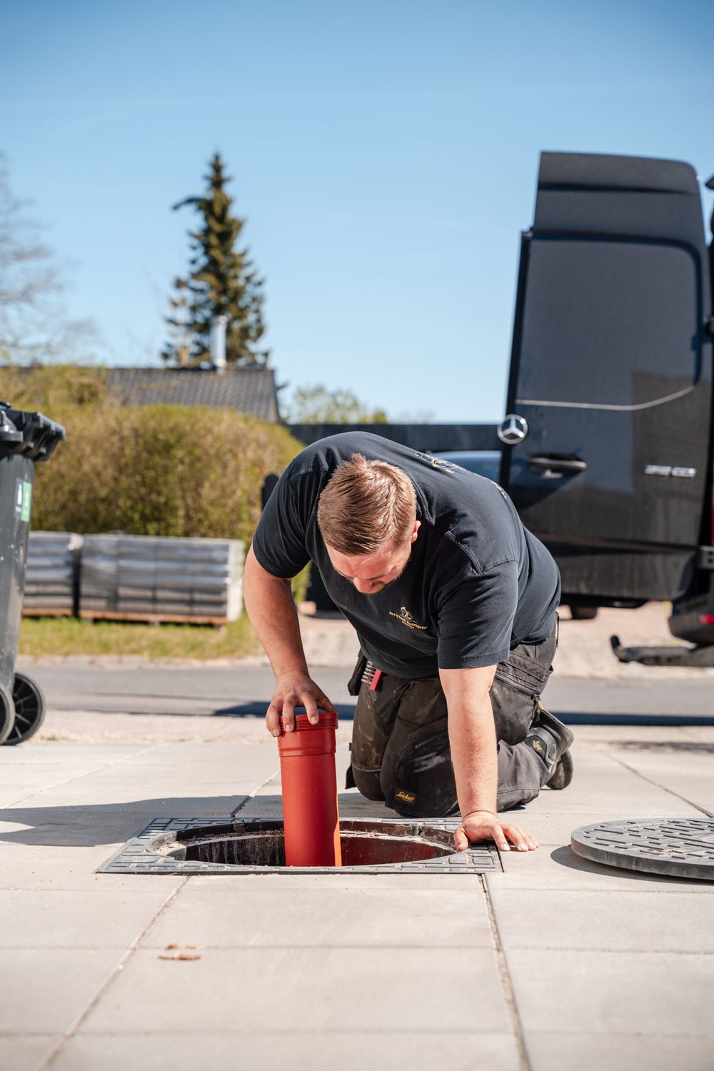 Rasmus på knæ ved en åben brønd i en indkørsel, dækslet er taget af